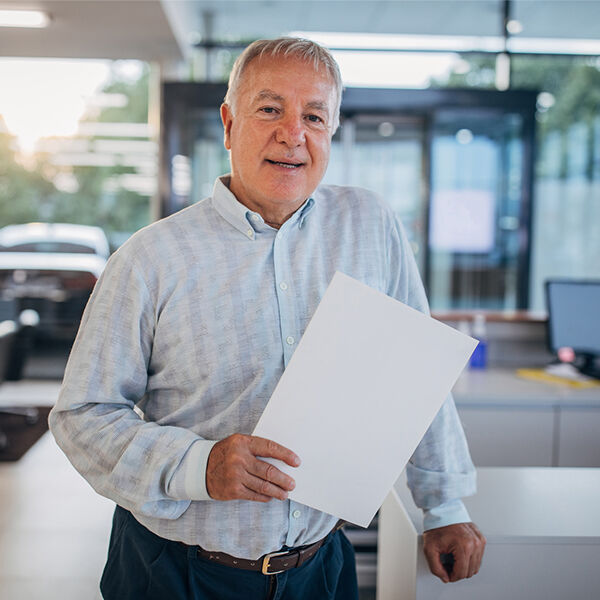 A car dealership owner stood in front of his desk holding paperwork