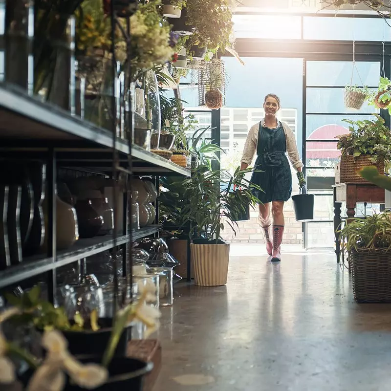 A Female garden centre employee caries plants through a shop aisle