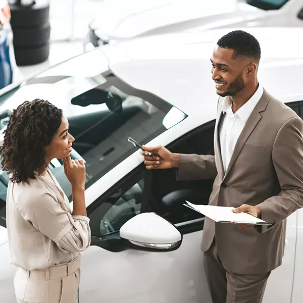 A woman is stood next to a new car talking to a car salesman