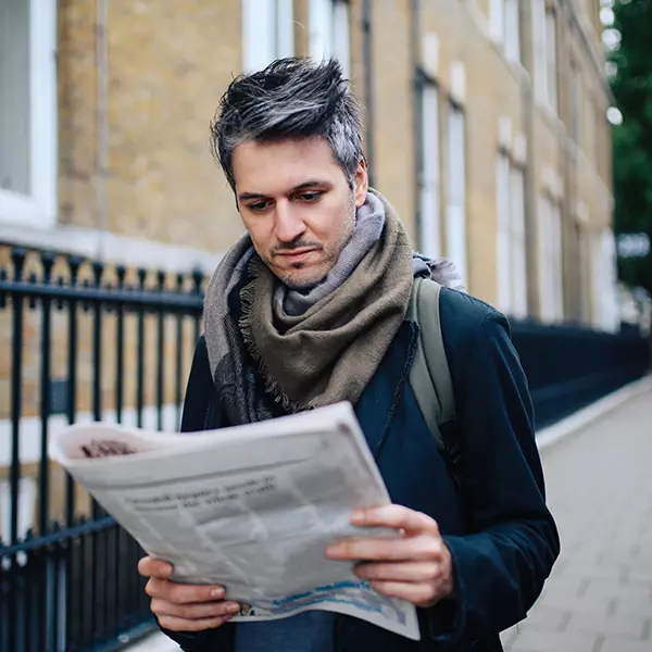Man reading newspaper while going for a walk